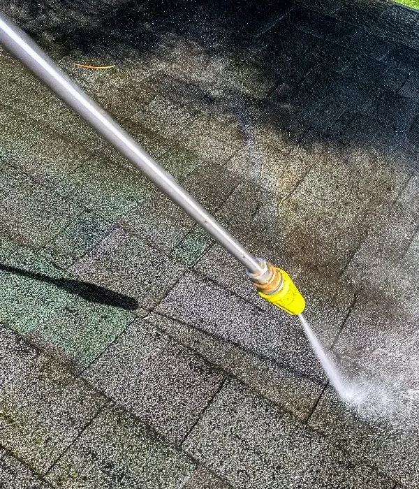 Pressure washing technician cleaning an asphalt shingle roof in Hoover, Alabama to remove dirt, algae, and stains.